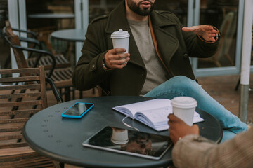 Close up shot of young businessman explaining and gesticulating with his hands. He is holding a cup...