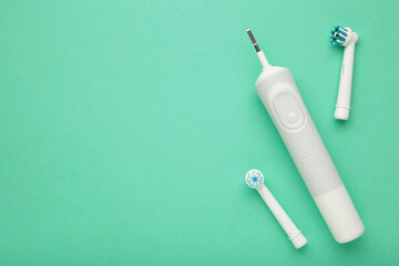 Naklejka premium Modern electric toothbrush with a few spare heads on mint background