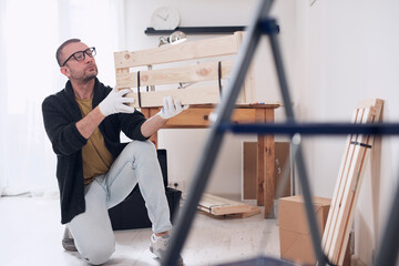 Man assembling new wooden shelf and furniture in the apartment.