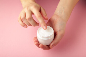 Close up woman hands holding bottle of white face cream on pink background. Skin care