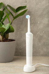 Electric toothbrush with green flower on grey background. Vertical photo