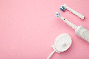Modern electric toothbrush with spare heads and charger on pink background