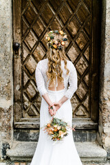 Wunderschöne Braut mit langen Haaren, Blumenkranz und Brautfrisur von hinten	vor alter Holztüre