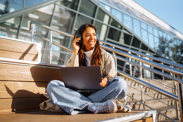 Young woman in headphones with a laptop on a city street. Online training, remote work and...