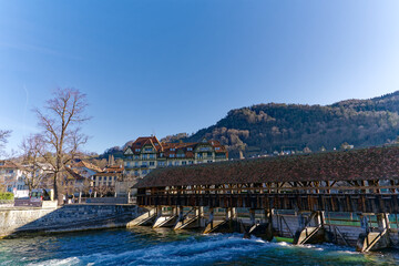 Scenic view of Aare River with close-up of barrier and covered wooden bridge at Swiss City of Thun on a sunny winter day. Photo taken February 21st, 2023, Thun, Switzerland.
