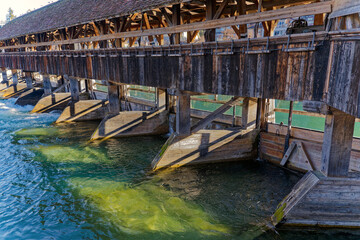 Fototapeta na wymiar Scenic view of Aare River with close-up of barrier and covered wooden bridge at Swiss City of Thun on a sunny winter day. Photo taken February 21st, 2023, Thun, Switzerland.