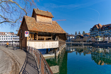 Fototapeta na wymiar Scenic view of Aare River with close-up of barrier and covered wooden bridge with beautiful reflections in water at Swiss City of Thun. Photo taken February 21st, 2023, Thun, Switzerland.