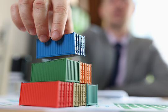 Business man arranging several cargo containers on his table with financial reports.