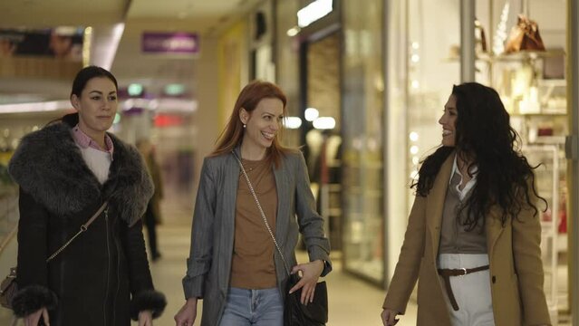 Stylish young women walking in shopping mall together while talking and smiling. Cheerful friends shopping in mall. Shot in slow-motion