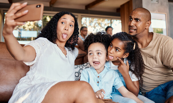 Family, funny face and selfie with tongue out in home, having fun and bonding together. Interracial, comic photography and father, mother and girls taking pictures for social media and happy memory.