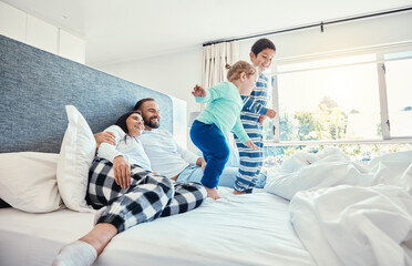 Family, morning and kids jumping on a bed, playing while having fun in the bedroom of their...