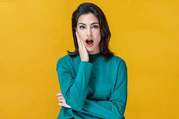 Surprised young woman screaming and putting her hands on her face looking at camera isolated on yellow