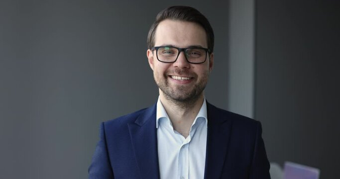 Head shot portrait happy successful millennial Caucasian businessman posing in office wear elegant formal suit and glasses smile staring at cam looks self-assured and satisfied with career in company