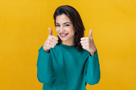 Beautiful young woman expressing happiness with thumb up isolated on yellow