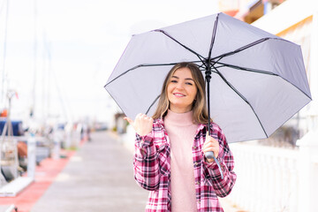 Young pretty Romanian woman holding an umbrella at outdoors pointing to the side to present a product