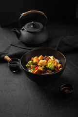 Vegetarian tofu bowl with vegetables and rice on black background