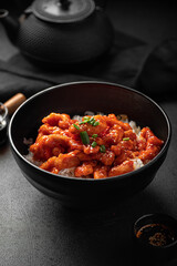 Portion of asian sweet spicy chicken with rice on black background