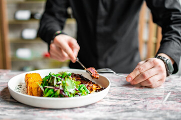 man hands with fork and knife eating beef steak and salad in cafe