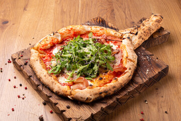 Oven baked pizza with mozzarella cheese, dried ham, tomatoes, balsamic vinegar and arugula