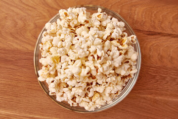 A bowl on a wooden background is completely filled with popcorn. A sweet snack.