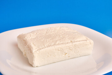 A slice of sour milk cheese on a white plate. Dairy business.