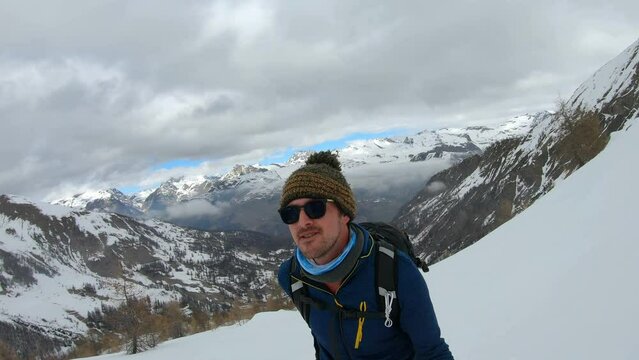 Man hiking with stick on splitboard in an environement composed of clouds moutanin forest and snow. Recorded in selfie view
