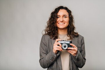 Ecstatic young curly woman wearing jacket is holding a vintage camera.