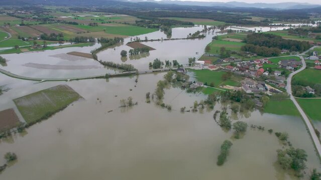 AERIAL: Extensive flooding of farmland after a rising river overflowed its banks. Muddy autumn flood water submerged green meadows and fields and came dangerously close to the residential houses.