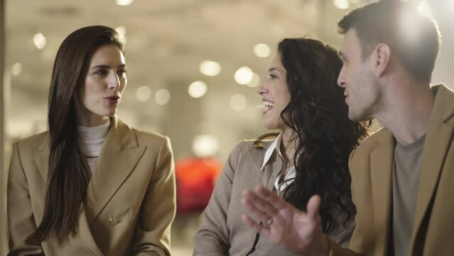 Close-up view of a group of male and female friends sitting on bench in the mall, discussing with each other in slow-motion