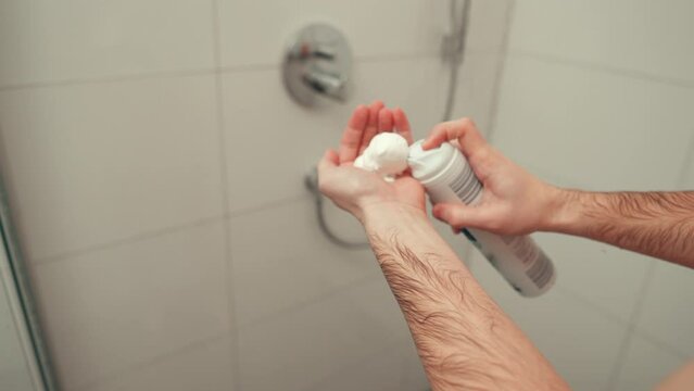 Man spraying shaving foam onto his hand while taking a shower.