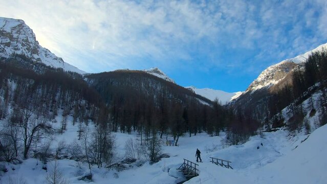 Man hiking with a splitboard in a majestic mountain landscape. He pass on a bridge.