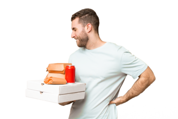 Young handsome blonde man holding pizzas and burgers over isolated background suffering from backache for having made an effort
