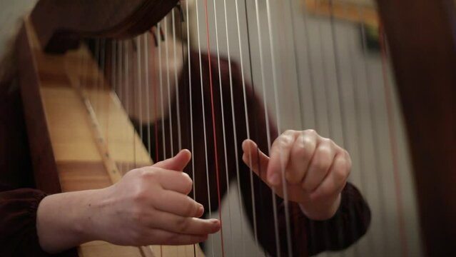Handheld footage with details of the hands of a woman playing a harp.