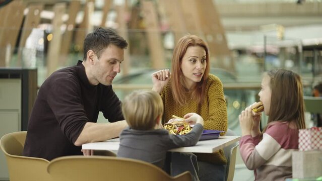 Married couple with kids having lunch during shopping. They are eating french fries and burger at caf� in slow-motion