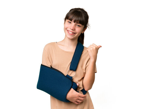 Little caucasian girl with broken arm and wearing a sling over isolated background pointing to the side to present a product