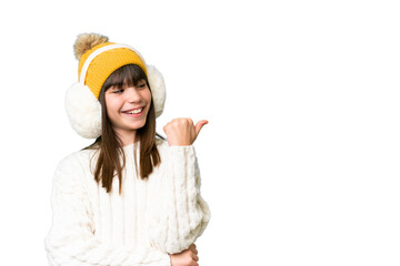Little caucasian girl wearing winter muffs over isolated background pointing to the side to present...