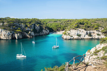 Beautiful beach with sailing boat yacht, Menorca island, Spain. Sailing boats in a bay. Summer fun, enjoying life, yachting, travel and active lifestyle concept - obrazy, fototapety, plakaty