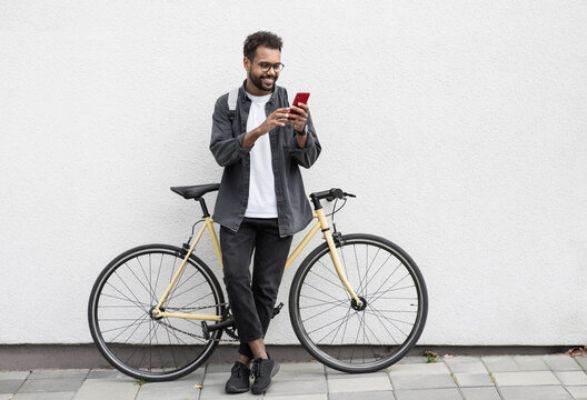 Young handsome man with bicycle over white wall background in a city, cheerful student men with mobile phone smiling outdoor, Modern healthy lifestyle, travel, casual business, connection concept