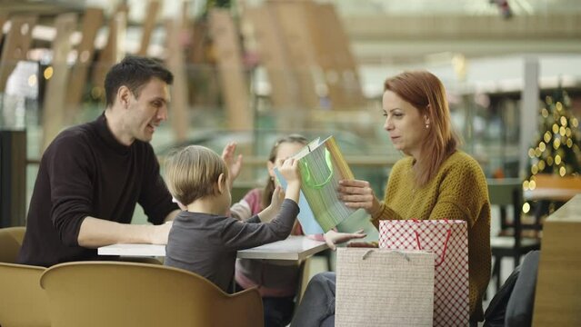 Parents and kids of a family eating together after shopping and having fun at the restaurant. Son and daughter checking shopping bag while eating