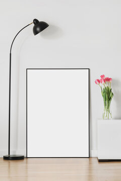 Blank picture frame mockup on white wall. White living room design. View of modern scandinavian style interior with artwork mock up standing on floor. Home staging and minimalism concept