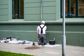 Maler und Lackierer arbeitet mit Pinsel und Farbe an einer Fassade und Regenrinne eines Hauses an...