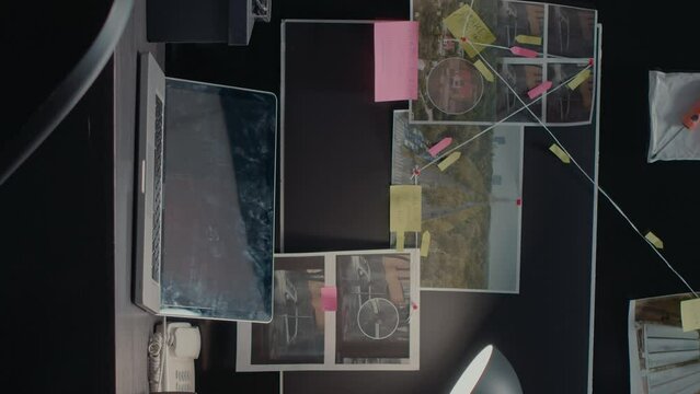 Vertical video: Detective board with clues over desk in police archive, crime scene photos connected on wall and case files in investigation office. Empty incident room with forensic evidence and