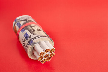 Cigarettes wrapped in 100 dollar bills on a red background. The concept of a constant increase in the price of cigarettes.
