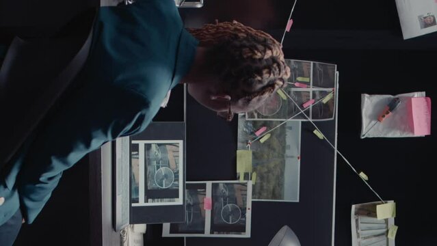 Vertical video: African american police investigator reading case file in incident room. Woman detective holding folder and analyzing investigation report, looking at criminal records to find suspect.