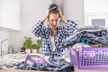Woman shouts from anger and holds her head as she is frustrated from house chores and the pile of clothes she needs to iron