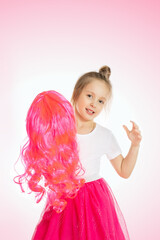 smiling little girl holding pink hair wig on pink background.