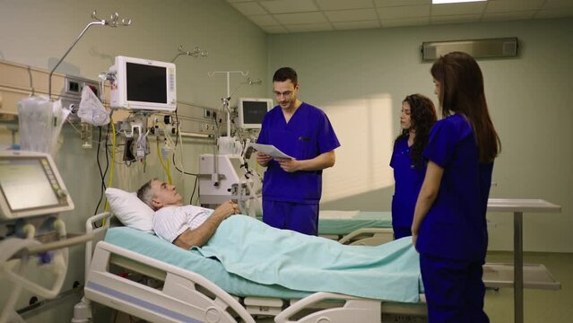 Doctor and nurses talking with a male patient who is lying on a bed in the hospital. Shot in slow-motion