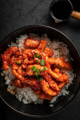 Portion of asian sweet spicy chicken with rice on black background