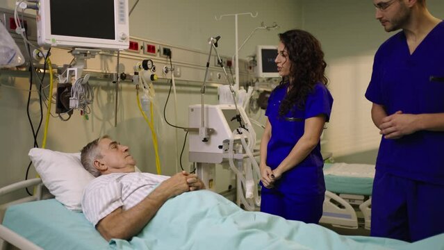 Slow-motion shot of female doctor and medical stuffs talking to male patient in hospital bed in hospital cabin