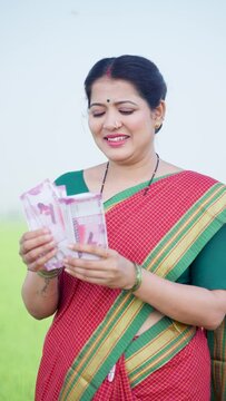 vertical shot of Happy smiling woman counting money near green farmland - concept of Earnings, banking or finanical support and woman empowerment or growth